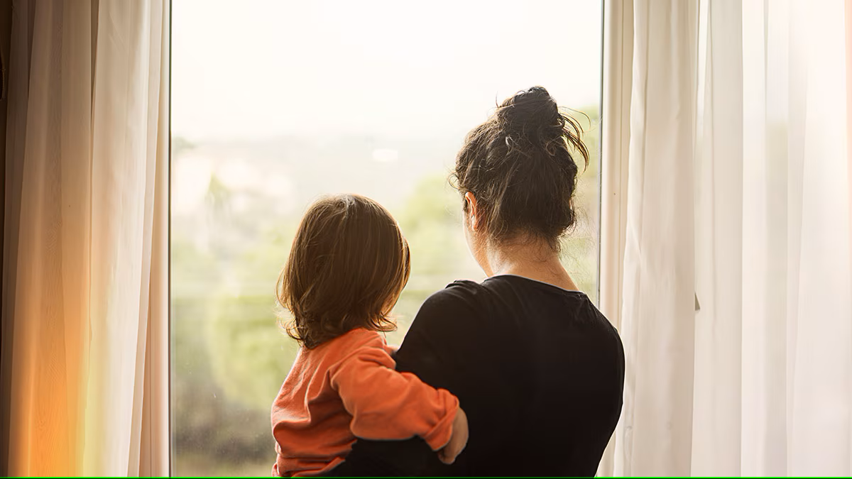 Mother and daughter looking out of a window into hazy air.